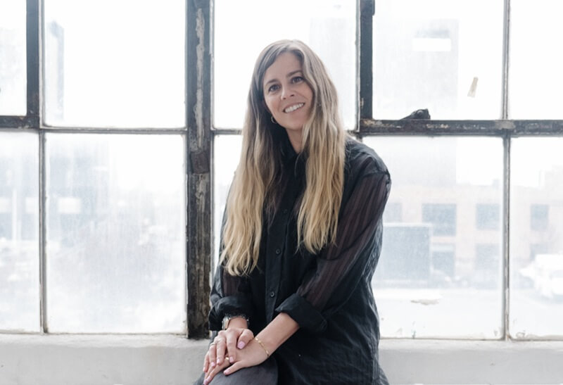 Clara Andrade Pereira, Executive Director of Untitled Art Fairs, seated by a loft window with a soft city backdrop.