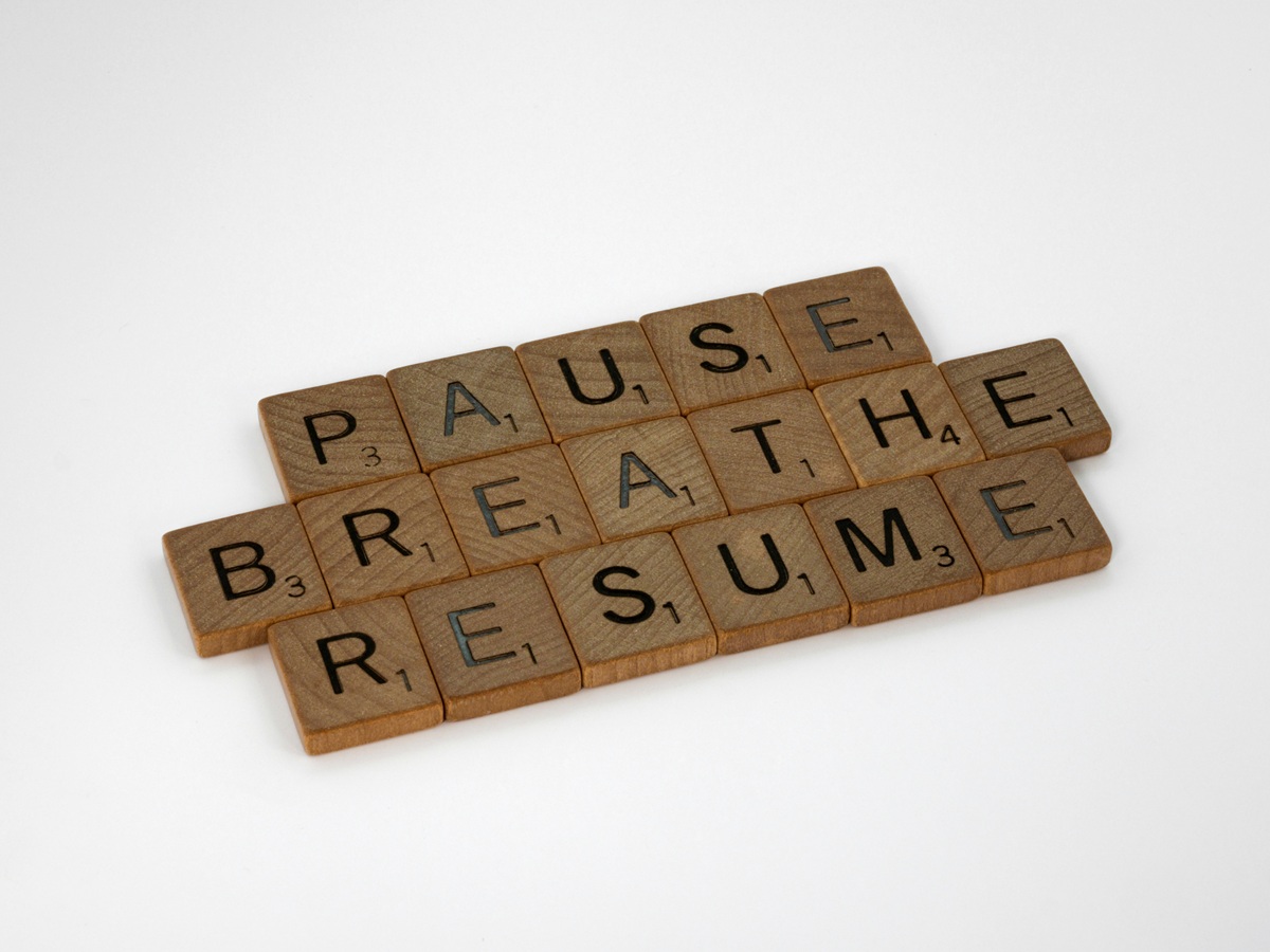 Scrabble tiles spelling the words ‘Pause’, ‘Breathe’, and ‘Resume’ arranged on a white background.